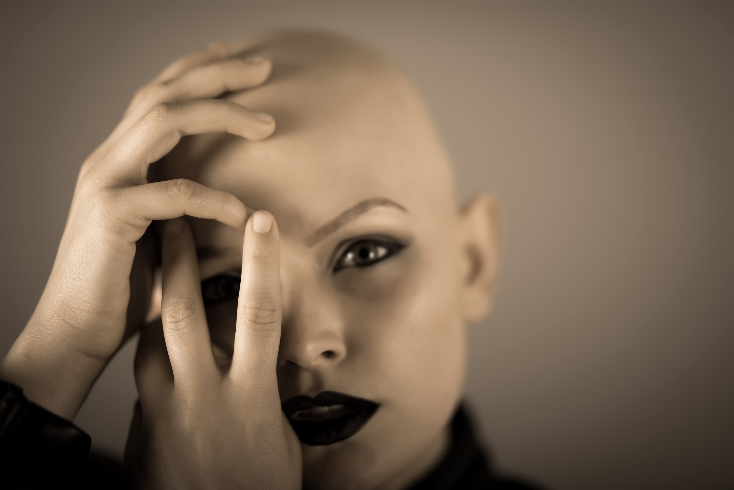 Emotive portrait of a beautiful bald woman while covering her face with her hands.